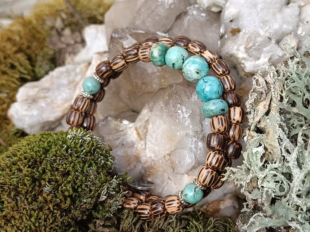 Crée avec des perles de palmier hagal et de turquoises africaines, ce bracelet rayonne les valeurs de l’apaisement, de l’union entre Ciel et Terre, réussite, chance et communication, sur acier inoxydable mémoire de forme en deux tours. Une pampille arbre de vie vient terminer ce bracelet... Palmier : Symbole de résurrection, associée au paradis, au Christ, à l'oiseau phénix, empreinte de merveilleux Valeurs de l’homme juste : élévation, abondance et flexibilité - Aide au calme Symbole de réussite, de croissance, de chance et de longévité Turquoise africaine : Elle est un minéral bleu-vert clair à foncé issue de la famille des Phosphates. Les principaux gisements de Turquoise se trouvent dans les pays suivants : la Chine, le Tibet, l'Egypte, l'Iran, l'Afghanistan et les Etats-Unis. La pierre Turquoise a une dureté qui se situe entre 5 et 6 sur l'échelle de Mohs. La Turquoise est une pierre de communication. Elle est considérée comme une pierre purificatrice et apaisante. Elle fluidifie la circulation sanguine et améliore les organes du corps. De plus, la pierre aide à régénérer et apaiser les blessures et les douleurs. La Turquoise peut également améliorer la gestion de l'alimentation. Sur le plan mental, elle est connue pour ses nombreux bienfaits communicatifs et régénérants. Elle fluidifie la parole et favorise l'expression de soi, la communication et surtout l'écoute des autres. La Turquoise apporte des bienfaits relaxants pour améliorer le sommeil. Enfin, on dit que cette pierre naturelle protège l'usager des mauvaises ondes. Elle permet de calmer les colères et développant l'empathie, et d'absorber les mauvaises énergies et de les convertir en énergies positives. La Turquoise est symbole d'union entre le ciel et la terre. La pierre Turquoise est associée aux chakras de la gorge qui amplifie la communication et favorise l'expression de soi. Celle-ci est aussi associée au chakra du cœur qui renforce les émotions positives telles que l'amour, la bienveillance et l'empathie.  Purification par la fumigation (encens ou sauge…), ou avec un bol de cristal ou tibétain, et recharge 2 à 3 heures dans une pièce baignée par le soleil.