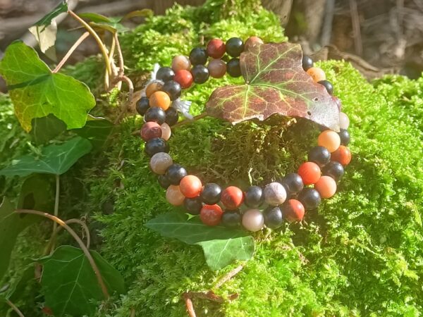 Crée avec des perles de bois d'ébène noir et des perles de bois pétrifié (ou bois fossile), ce bracelet, monté en deux tours sur une base d'acier inoxydable mémoire de forme, rayonne les énergies du lâcher prise, de la patience et de l'ancrage. Une pampille arbre de vie vient terminer ce bracelet sur une touche d'ancrage supplémentaire. Le bois pétrifié  favorise l’attention et centre l’énergie, la patience et le lâcher-prise, l’accès à notre conscience, il encourage la transmission et favorise l’ancrage. Il permet tout d’abord de favoriser l’attention d’une personne afin qu’elle soit moins distraite. Il est ainsi particulièrement conseillé pour les enfants agités, parfois hyperactifs, car il les ramène à plus de stabilité et contrôle. Le bois fossilisé est aussi indiqué pour vous guider et vous apprendre la patience et le lâcher-prise. Il permet de vous stabiliser, et de vous débarrasser de chaque information négative, comme des croyances limitatrices. Grâce à son parcours, ayant traversé les âges, il vous permet de reprendre contact avec vos codes identitaires profonds. Vous pouvez ainsi aborder les événements, si divers et inattendus soient-ils, avec une distance suffisante. En vous donnant cette force de recul, ce courage, ce bois vous permet d’accéder à une sérénité profonde, quels que soient les aléas de votre quotidien, tout en vous restituant votre spontanéité. Vous pouvez atteindre un haut niveau de sagesse et de courage, et vous rayonnerez naturellement au quotidien. Liés aux Mystères de la Vie, ainsi qu’à vos connaissances profondes, ce bois pierre de grande qualité vous donne accès au monde, en vous permettant de relâcher votre volonté et votre contrôle mental. Ainsi, vous pouvez vous inscrire de façon profonde dans votre propre réalité et vos projets seront plus facilement matérialisés. Ce bois va développer en vous une envie profonde de propre transmission, en développant vos intuitions ainsi que votre communication sensorielle avec les éléments de la Nature. Vous vivez alors le moment présent, en totale connexion avec votre personne et le monde qui vous entoure. En favorisant l’ancrage, l’enracinement, la connaissance, votre corps va réintégrer sa place dans la nature, loin des rêveries ou d’un mental trop pesant. En stimulant le chakra racine, vous allez revenir aux fondamentaux, vous détachant de chaque chose matérielle. En favorisant un lien avec vos ancêtres et vos origines, vous allez pouvoir communiquer lors de séance de méditation de transes hypnotiques ou encore de rêves lucides. Vous allez naturellement établir un lien avec le savoir des Anciens. On attribue aussi à ce bois des vertus de longévité, la persévérance, la patience, ainsi que le gain de force et de courage pour affronter les différentes épreuves. En favorisant la reconnaissance des petits bonheurs de la vie, ce fossile produit un bonheur simple et de qualité, en rendant beau chaque instant. Il procure aussi lucidité et clarté. Il s’adresse particulièrement aux personnes trop actives, qui n’arrivent plus à se connecter avec leur moi-intérieur, ou qui s’attardent trop sur les choses matérielles. Et également à celles souhaitant entrer méditation ou dans un état de transe poussée afin de se reconnecter à leurs origines. Sur le plan physique, Le bois pétrifié soulage votre corps grâce à son action de renforcement sur l’ossature, les tendons, et les articulations. C’est un soutien idéal pour les troubles dégénératifs. Ce bois est préconisé pour une utilisation par les séniors. En effet, c’est une excellente protection contre les fractures osseuses. Mais il est aussi idéal pour les plus petits, car il favorise la croissance physique et intellectuelle. Il agit aussi en cas de fatigue chronique ou de trouble profond. Il donne de plus énergie et vitalité, favorise la croissance des os, et renforce les organes tels que le cœur ou la rate. Il aide aussi à la fortification du système nerveux. Symbolique de la pierre bois fossile : Le bois pétrifié représente la sagesse maternelle (Terre-Mère) et les sciences surhumaines. L’ébène naturelle est le nom donné au bois de cœur produit par plusieurs espèces d’arbres de la famille des Ebenaceae appartenant au genre Diospyros, appelés ébéniers, ainsi que certains arbres du genre Dalbergia. Ils se rencontrent dans les régions tropicales de l’Ancien Monde et sont connus depuis la plus haute Antiquité pour la couleur très sombre, proche du noir, de leur bois.Symbole de puissance, de pureté, de protection et de chance. Depuis l’antiquité on lui attribue de nombreuses propriétés magiques. Telles que chasser les mauvais esprits et les démons. La croyance veut aussi que le bois d’ébène soit un grand réceptacle des énergies magiques, aussi on y enfermait dans des coffres en ébène les objets magiques. L’ébène est le bois le plus puissant en magie et divination. Son pouvoir est général, rien ne lui résiste et il agit dans tous les domaines. Très protecteur, il convient mieux aux expérimentés. Les bijoux en bois d’ébène apporteraient courage, force et agilité. La couleur noire, la profondeur et la protection. L’arbre de vie : D’une jeune pousse devenue un grand arbre majestueux, il évoque l’énergie de la vie. L’arbre de vie peut donc être comparé à l’Homme qui grandit au fil du temps et de ses expériences. Chez les chrétiens, il est souvent associé à l’amour de Dieu et évoque sa protection. Symbole universel et intemporel, l’arbre de vie constitue une représentation particulièrement puissante du cycle de la vie. Ses racines représentent les origines qui s’ancrent à la terre où il puise son énergie. Ses branches symbolisent le développement de la vie tandis que ses feuilles évoquent l’épanouissement et l’accomplissement de soi. L’arbre de vie peut représenter l’homme durant le cycle de sa vie, de sa naissance à sa mort. Dans de nombreuses religions et civilisations, l’arbre de vie revêt d’un symbolisme particulier et propre à chacun. Mais toutes les croyances s’accordent sur le fait que l’arbre de vie symbolise entre autres la renaissance, l’amour et la protection. Il est également symbole d’énergie, de sagesse et de longévité. Purification par la fumigation (encens ou sauge…), ou avec un bol de cristal ou tibétain, et recharge 2 à 3 heures dans une pièce baignée par le soleil