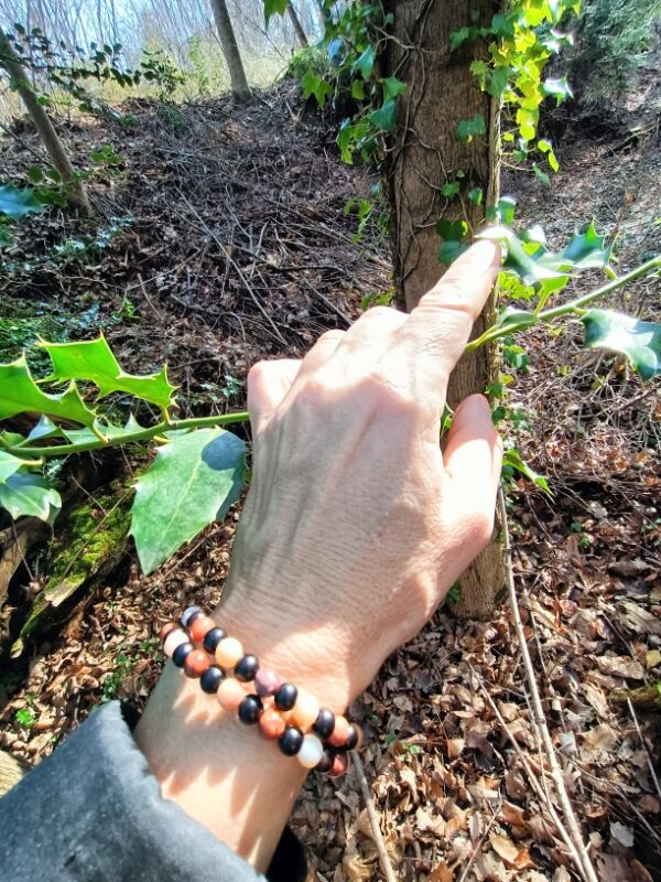 Crée avec des perles de bois d'ébène noir et des perles de bois pétrifié (ou bois fossile), ce bracelet, monté en deux tours sur une base d'acier inoxydable mémoire de forme, rayonne les énergies du lâcher prise, de la patience et de l'ancrage. Une pampille arbre de vie vient terminer ce bracelet sur une touche d'ancrage supplémentaire. Le bois pétrifié  favorise l’attention et centre l’énergie, la patience et le lâcher-prise, l’accès à notre conscience, il encourage la transmission et favorise l’ancrage. Il permet tout d’abord de favoriser l’attention d’une personne afin qu’elle soit moins distraite. Il est ainsi particulièrement conseillé pour les enfants agités, parfois hyperactifs, car il les ramène à plus de stabilité et contrôle. Le bois fossilisé est aussi indiqué pour vous guider et vous apprendre la patience et le lâcher-prise. Il permet de vous stabiliser, et de vous débarrasser de chaque information négative, comme des croyances limitatrices. Grâce à son parcours, ayant traversé les âges, il vous permet de reprendre contact avec vos codes identitaires profonds. Vous pouvez ainsi aborder les événements, si divers et inattendus soient-ils, avec une distance suffisante. En vous donnant cette force de recul, ce courage, ce bois vous permet d’accéder à une sérénité profonde, quels que soient les aléas de votre quotidien, tout en vous restituant votre spontanéité. Vous pouvez atteindre un haut niveau de sagesse et de courage, et vous rayonnerez naturellement au quotidien. Liés aux Mystères de la Vie, ainsi qu’à vos connaissances profondes, ce bois pierre de grande qualité vous donne accès au monde, en vous permettant de relâcher votre volonté et votre contrôle mental. Ainsi, vous pouvez vous inscrire de façon profonde dans votre propre réalité et vos projets seront plus facilement matérialisés. Ce bois va développer en vous une envie profonde de propre transmission, en développant vos intuitions ainsi que votre communication sensorielle avec les éléments de la Nature. Vous vivez alors le moment présent, en totale connexion avec votre personne et le monde qui vous entoure. En favorisant l’ancrage, l’enracinement, la connaissance, votre corps va réintégrer sa place dans la nature, loin des rêveries ou d’un mental trop pesant. En stimulant le chakra racine, vous allez revenir aux fondamentaux, vous détachant de chaque chose matérielle. En favorisant un lien avec vos ancêtres et vos origines, vous allez pouvoir communiquer lors de séance de méditation de transes hypnotiques ou encore de rêves lucides. Vous allez naturellement établir un lien avec le savoir des Anciens. On attribue aussi à ce bois des vertus de longévité, la persévérance, la patience, ainsi que le gain de force et de courage pour affronter les différentes épreuves. En favorisant la reconnaissance des petits bonheurs de la vie, ce fossile produit un bonheur simple et de qualité, en rendant beau chaque instant. Il procure aussi lucidité et clarté. Il s’adresse particulièrement aux personnes trop actives, qui n’arrivent plus à se connecter avec leur moi-intérieur, ou qui s’attardent trop sur les choses matérielles. Et également à celles souhaitant entrer méditation ou dans un état de transe poussée afin de se reconnecter à leurs origines. Sur le plan physique, Le bois pétrifié soulage votre corps grâce à son action de renforcement sur l’ossature, les tendons, et les articulations. C’est un soutien idéal pour les troubles dégénératifs. Ce bois est préconisé pour une utilisation par les séniors. En effet, c’est une excellente protection contre les fractures osseuses. Mais il est aussi idéal pour les plus petits, car il favorise la croissance physique et intellectuelle. Il agit aussi en cas de fatigue chronique ou de trouble profond. Il donne de plus énergie et vitalité, favorise la croissance des os, et renforce les organes tels que le cœur ou la rate. Il aide aussi à la fortification du système nerveux. Symbolique de la pierre bois fossile : Le bois pétrifié représente la sagesse maternelle (Terre-Mère) et les sciences surhumaines. L’ébène naturelle est le nom donné au bois de cœur produit par plusieurs espèces d’arbres de la famille des Ebenaceae appartenant au genre Diospyros, appelés ébéniers, ainsi que certains arbres du genre Dalbergia. Ils se rencontrent dans les régions tropicales de l’Ancien Monde et sont connus depuis la plus haute Antiquité pour la couleur très sombre, proche du noir, de leur bois.Symbole de puissance, de pureté, de protection et de chance. Depuis l’antiquité on lui attribue de nombreuses propriétés magiques. Telles que chasser les mauvais esprits et les démons. La croyance veut aussi que le bois d’ébène soit un grand réceptacle des énergies magiques, aussi on y enfermait dans des coffres en ébène les objets magiques. L’ébène est le bois le plus puissant en magie et divination. Son pouvoir est général, rien ne lui résiste et il agit dans tous les domaines. Très protecteur, il convient mieux aux expérimentés. Les bijoux en bois d’ébène apporteraient courage, force et agilité. La couleur noire, la profondeur et la protection. L’arbre de vie : D’une jeune pousse devenue un grand arbre majestueux, il évoque l’énergie de la vie. L’arbre de vie peut donc être comparé à l’Homme qui grandit au fil du temps et de ses expériences. Chez les chrétiens, il est souvent associé à l’amour de Dieu et évoque sa protection. Symbole universel et intemporel, l’arbre de vie constitue une représentation particulièrement puissante du cycle de la vie. Ses racines représentent les origines qui s’ancrent à la terre où il puise son énergie. Ses branches symbolisent le développement de la vie tandis que ses feuilles évoquent l’épanouissement et l’accomplissement de soi. L’arbre de vie peut représenter l’homme durant le cycle de sa vie, de sa naissance à sa mort. Dans de nombreuses religions et civilisations, l’arbre de vie revêt d’un symbolisme particulier et propre à chacun. Mais toutes les croyances s’accordent sur le fait que l’arbre de vie symbolise entre autres la renaissance, l’amour et la protection. Il est également symbole d’énergie, de sagesse et de longévité. Purification par la fumigation (encens ou sauge…), ou avec un bol de cristal ou tibétain, et recharge 2 à 3 heures dans une pièce baignée par le soleil